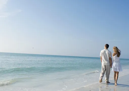 Пара гуляет по пляжу за руку